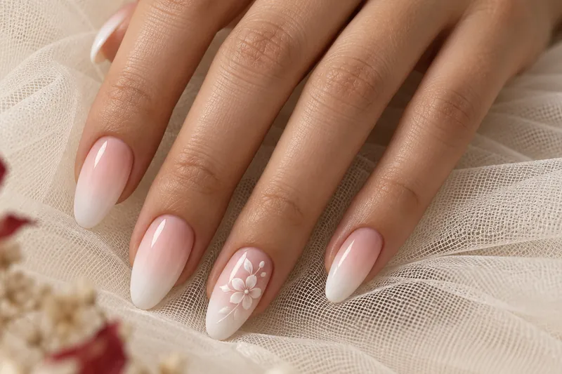Macro d'une main posée sur un tulle ivoire, ongles amande en baby boomer rose nacré et blanc, une petite fleur blanche peinte à la main sur l'annulaire, quelques pétales séchés flous au premier plan, lumière naturelle très douce, aucun visage